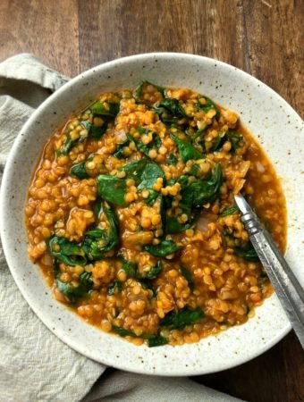 white bowl of soup with fresh spinach and spoon
