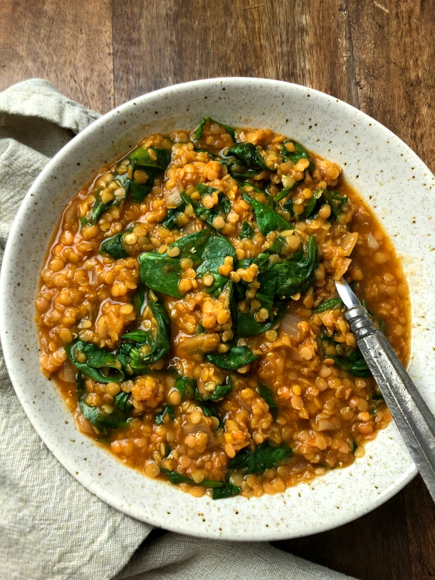 white bowl of soup with fresh spinach and spoon