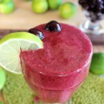 cherry lime slushie in large glass with lime slice