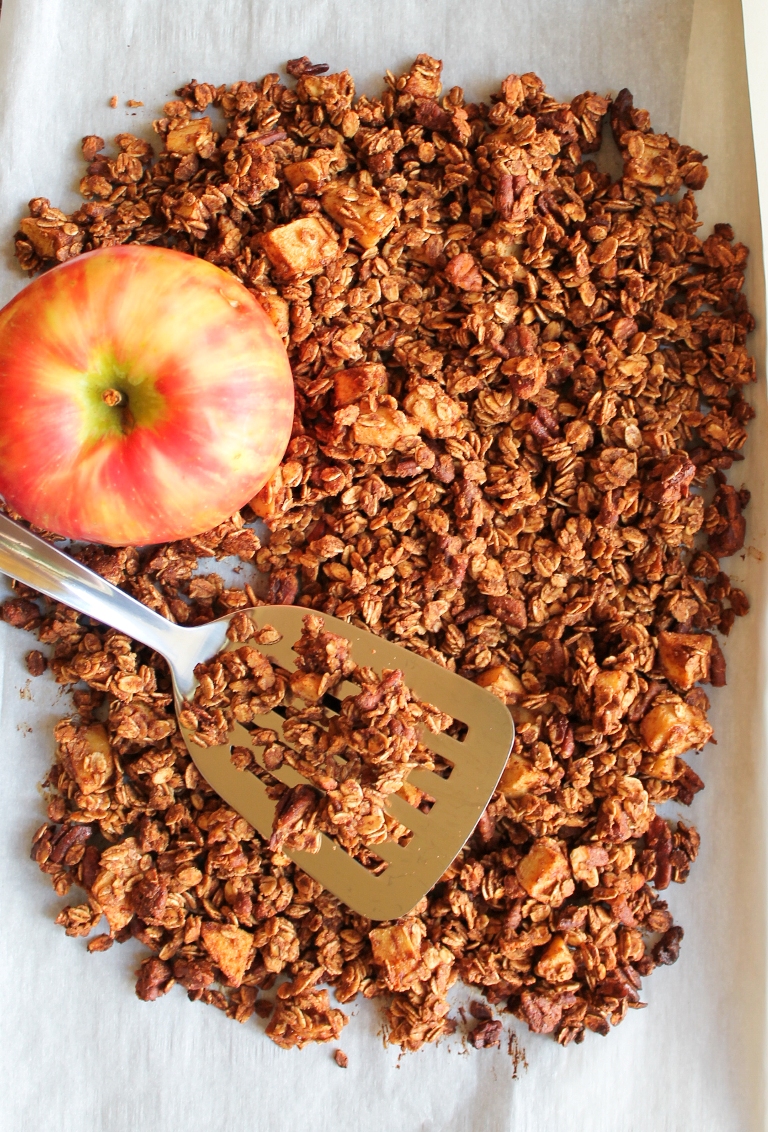granola spread out on pan with spatula and whole apple