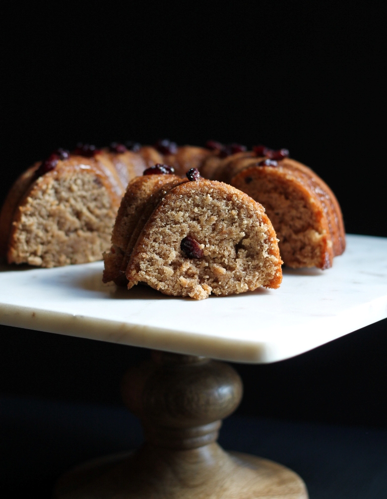 White cake stand showing slice of vegan cranberry bundt cake