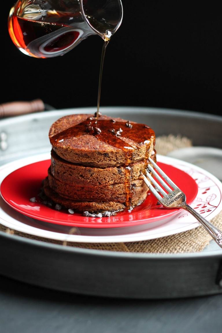 syrup pouring over stack of vegan pumpkin pancakes on red plate