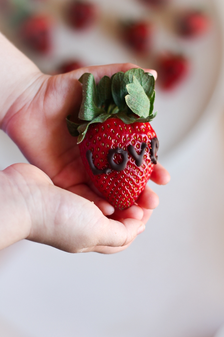 Little girl hands holding a strawberry with chocolate