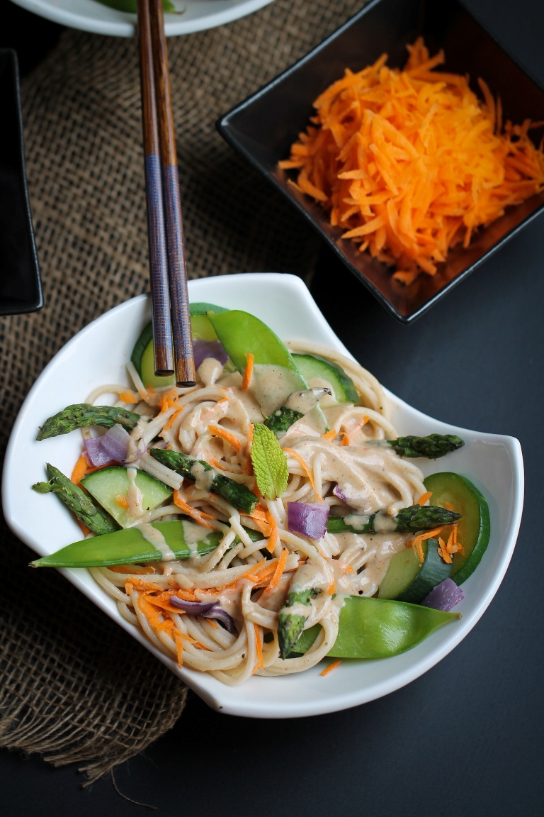 white bowl of buckwheat noodles with almond sauce and snow peas