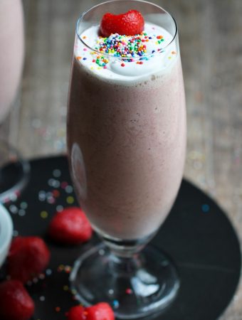 strawberry milkshake in tall glass with sprinkles