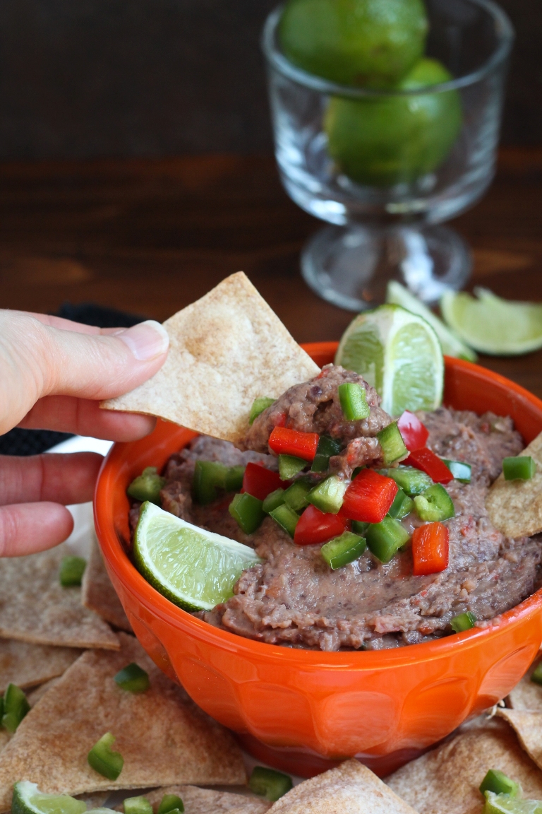 Hand dipping a chip into a bowl of smoky jalapeno black bean dip