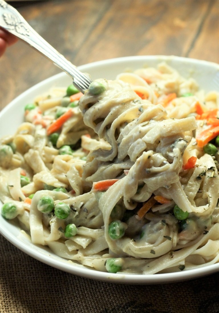 fork twirling alfredo sauce and fettuccini with peas and carrots