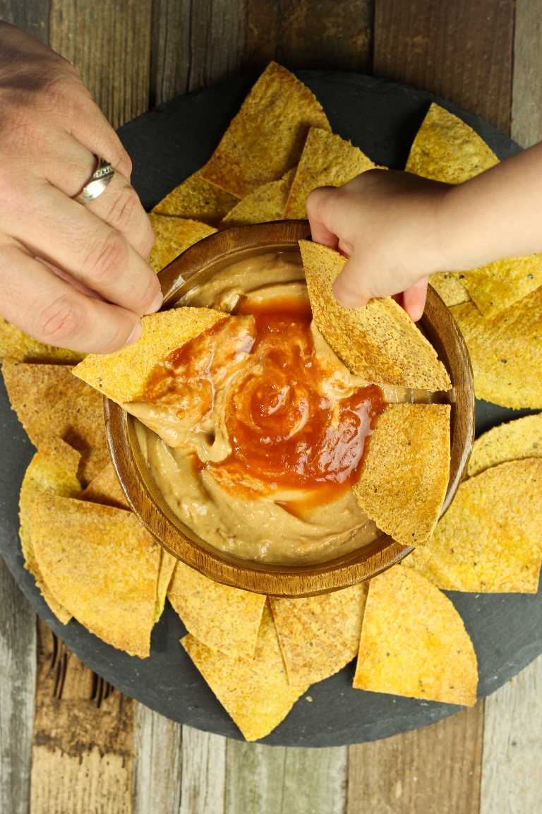2 hands dipping chips into wood bowl of cheese