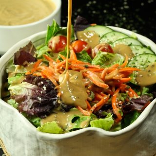 pouring vegan tahini goddess dressing over salad