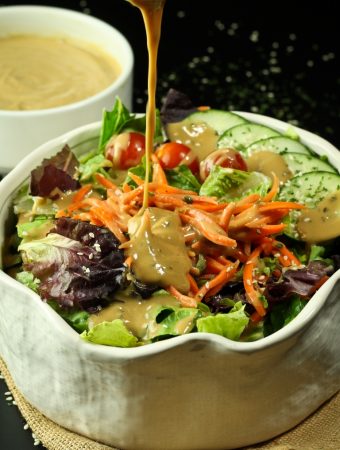 pouring vegan tahini goddess dressing over salad