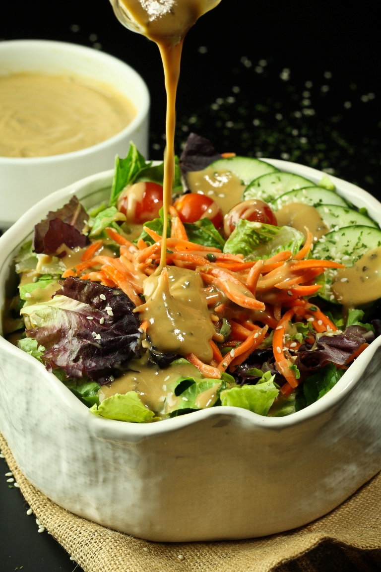 pouring vegan tahini goddess dressing over salad