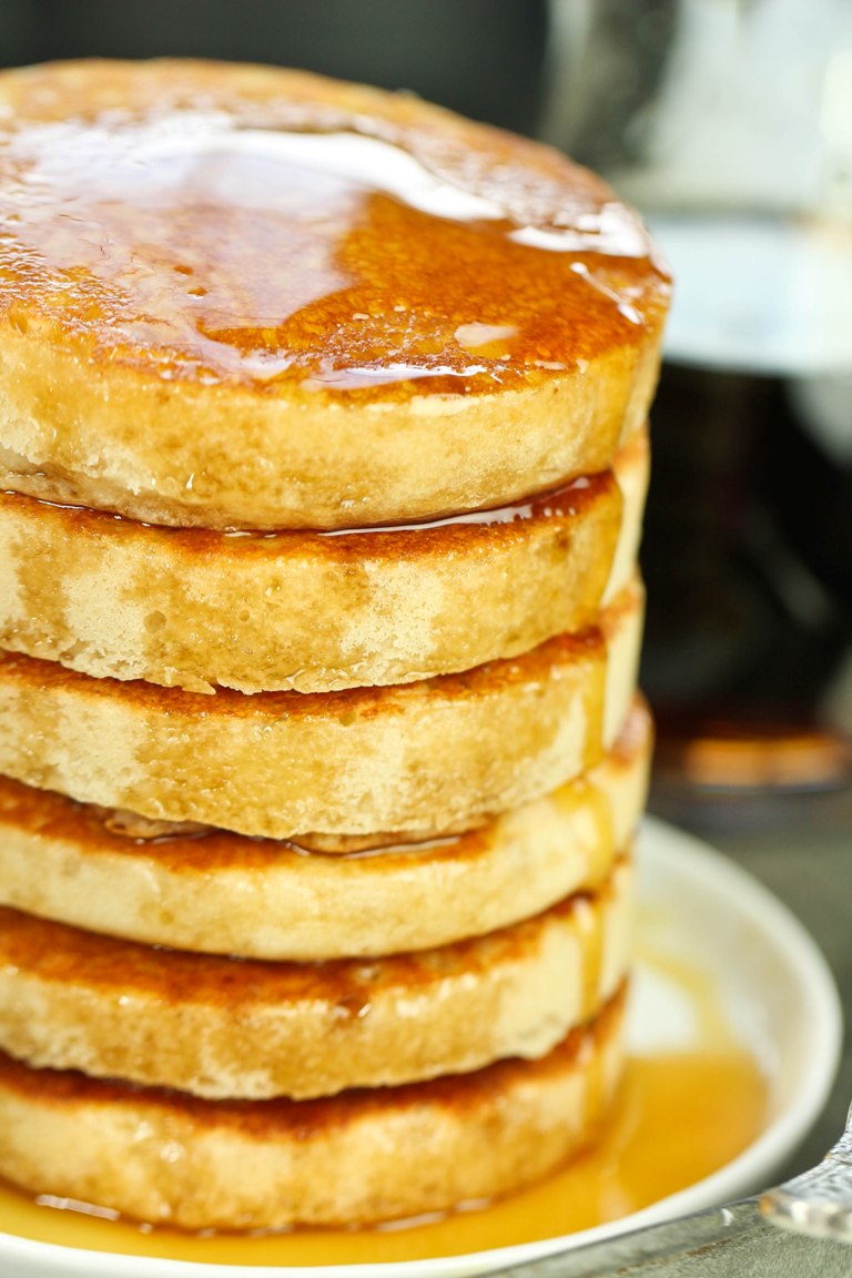 Tall stack of fluffy vegan buttermilk pancakes with syrup on top.