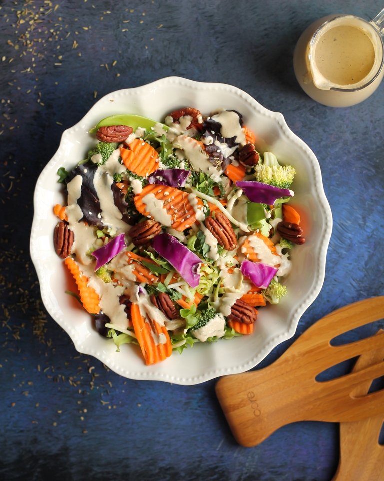 White bowl with large salad, carrots, pecans and vegan creamy Italian dressing.