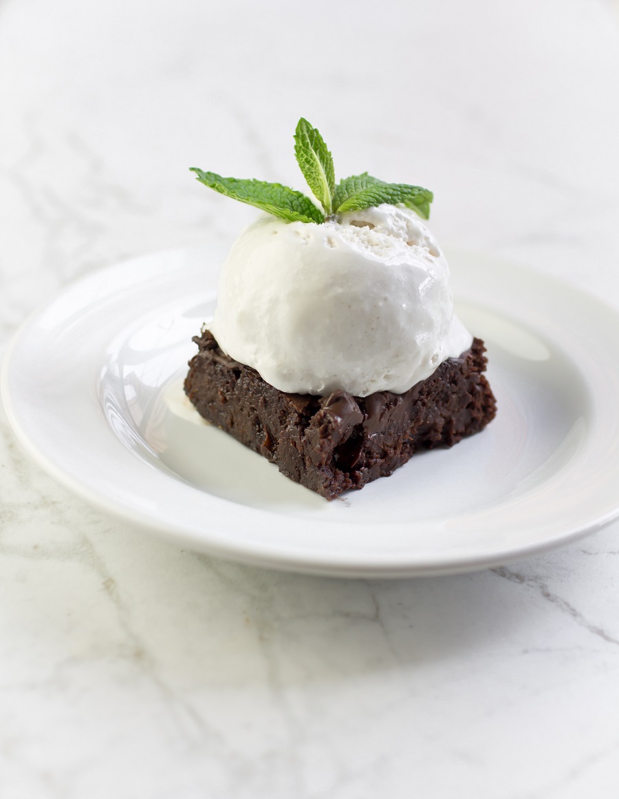 vegan gluten free zucchini brownie on white plate with whipped cream on top