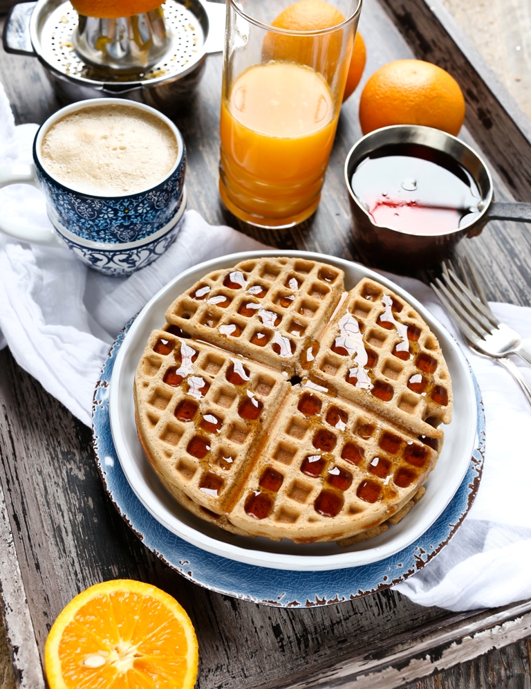 Plate of vegan chai waffles with syrup and orange juice