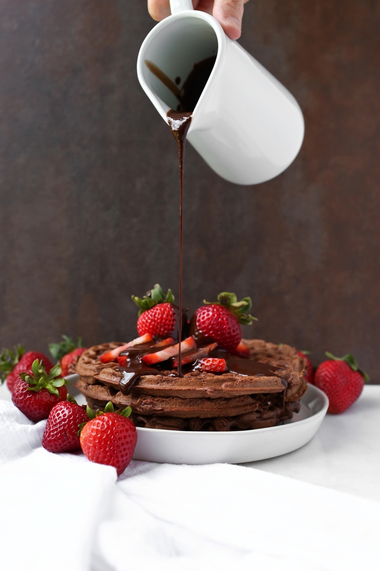 Chocolate syrup pouring over plate of chocolate waffles
