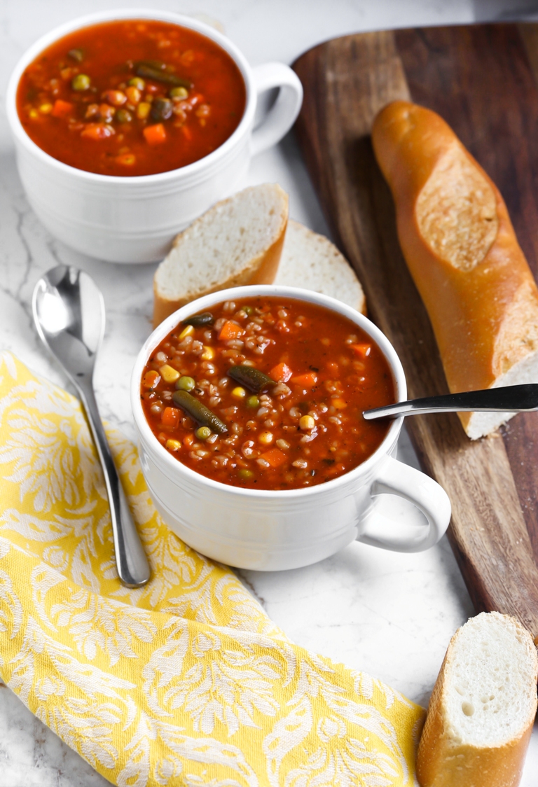 2 bowls of tomato rice vegetable soup with bread on side