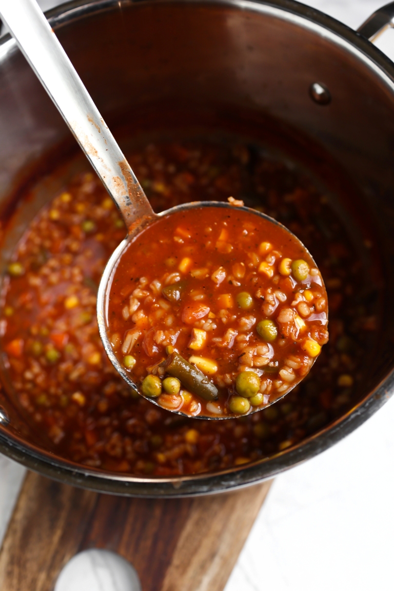 Ladle coming out of pot showing tomato vegetable soup