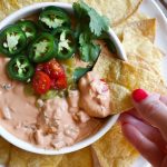 Vegan queso dip with hand dipping a chip in.