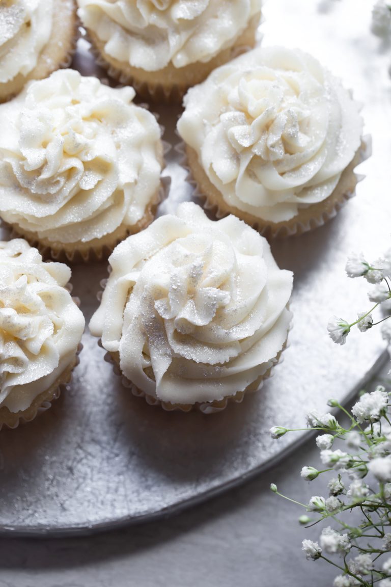Silver platter of several vegan white wedding cupcakes with white frosting.