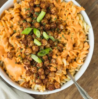 Closeup of plate of vegan pimento cream sauce over fusilli pasta with smoky chicpeas and green onions.