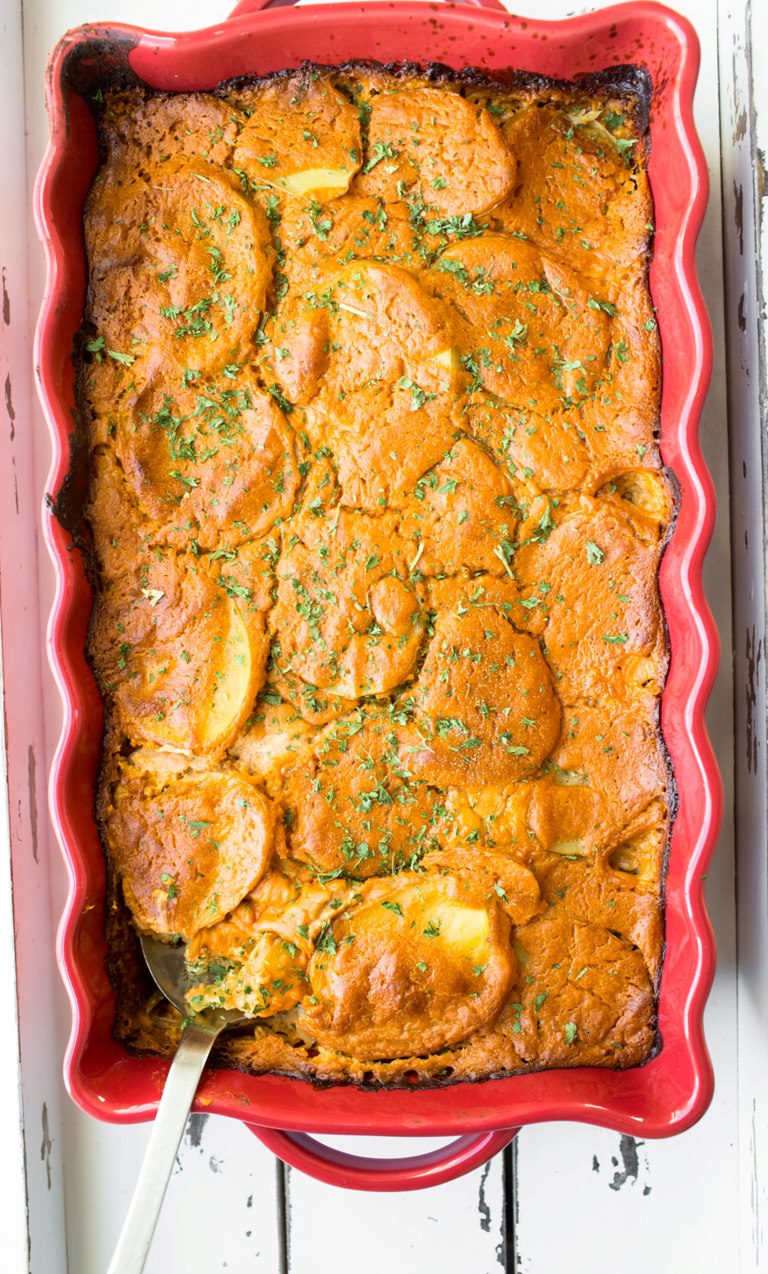 Large red casserole dish of baked vegan scalloped potatoes.