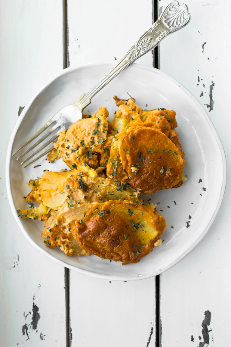 White plate of vegan scalloped potatoes with a fork on a white table.