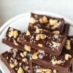 stack of vegan fudge pieces with walnuts and flaked sea salt on plate