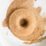 Vegan cinnamon sugar donut in bowl of sugar