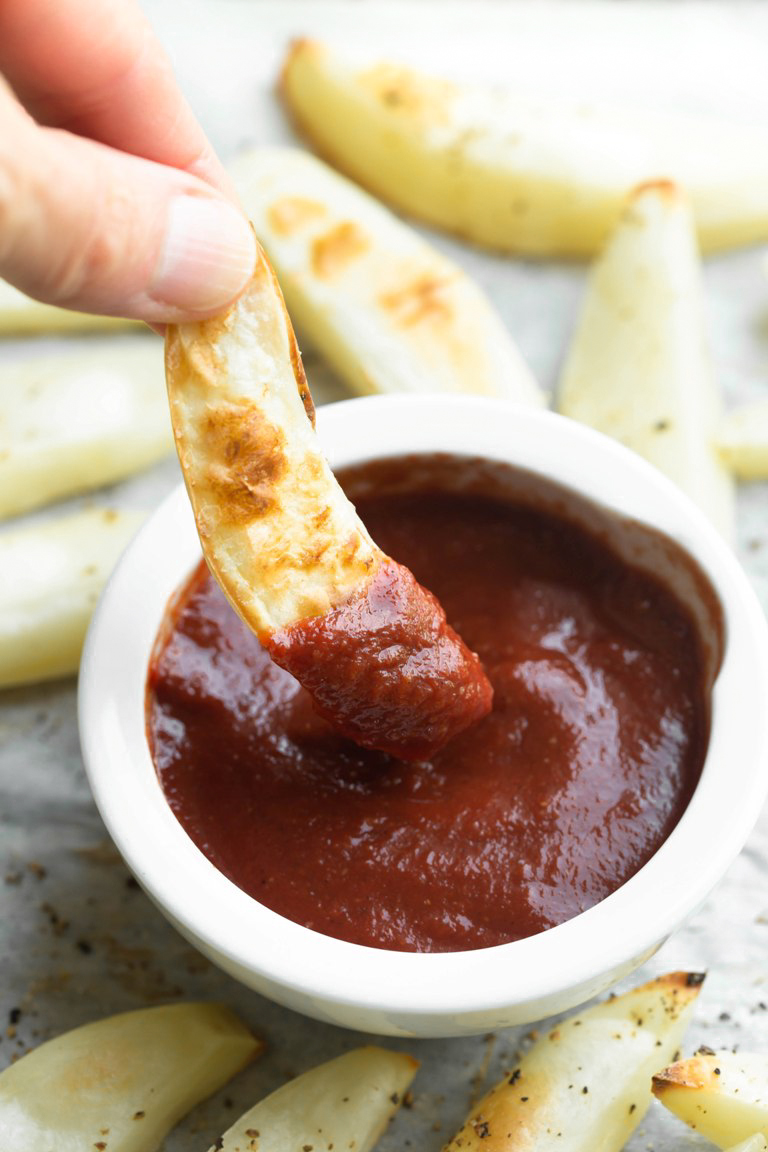 hand dipping fry into bowl of ketchup