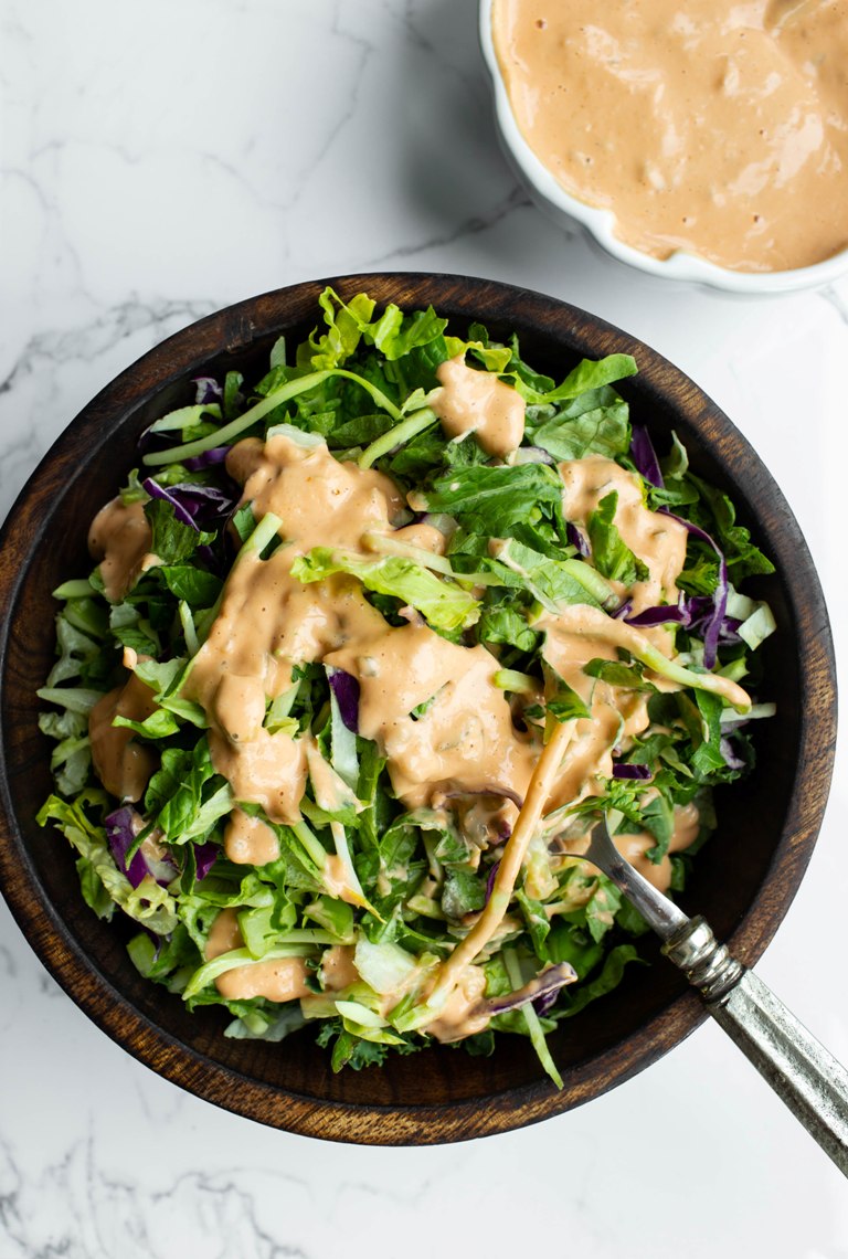 wooden bowl of salad with vegan thousand island dressing drizzled on top