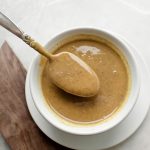 spoon holding smooth walnut butter above white bowl