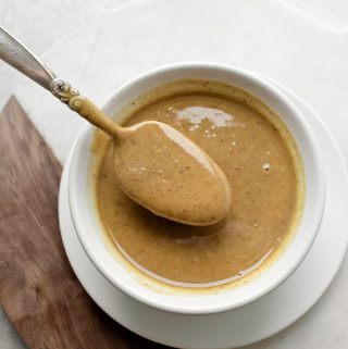 spoon holding smooth walnut butter above white bowl