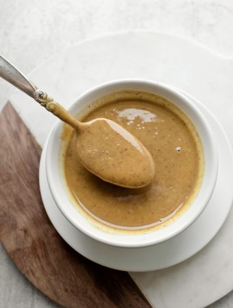 spoon holding smooth walnut butter above white bowl