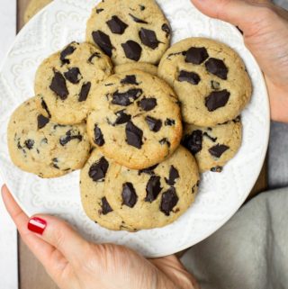 2 hands holding white plate of cashew butter cookies