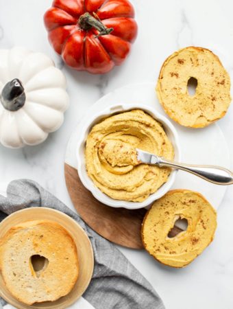 overhead shot of bowl of pumpkin cream cheese with bagels and mini pumpkins