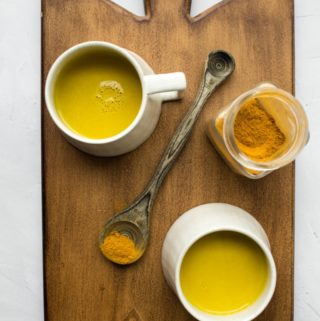 2 golden milk mugs with spices on wood board