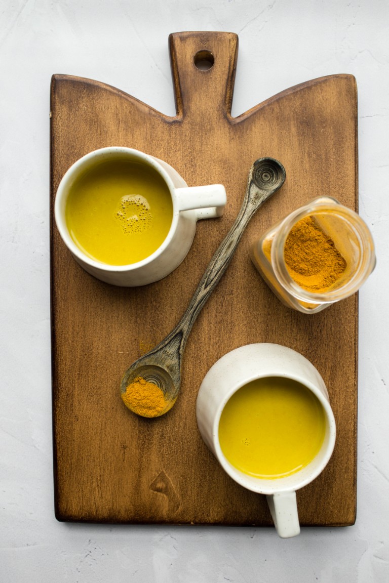 2 golden milk mugs with spices on wood board