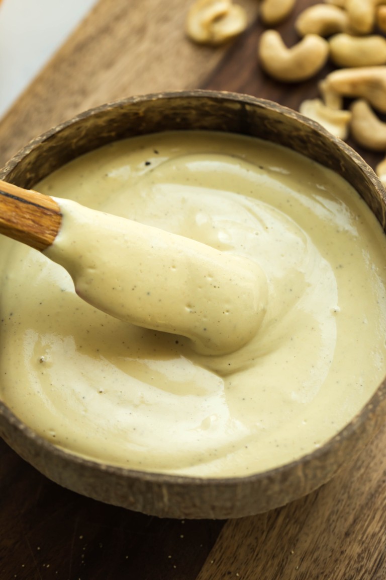 closeup of wooden spoon dipping into caesar dressing in wooden bowl