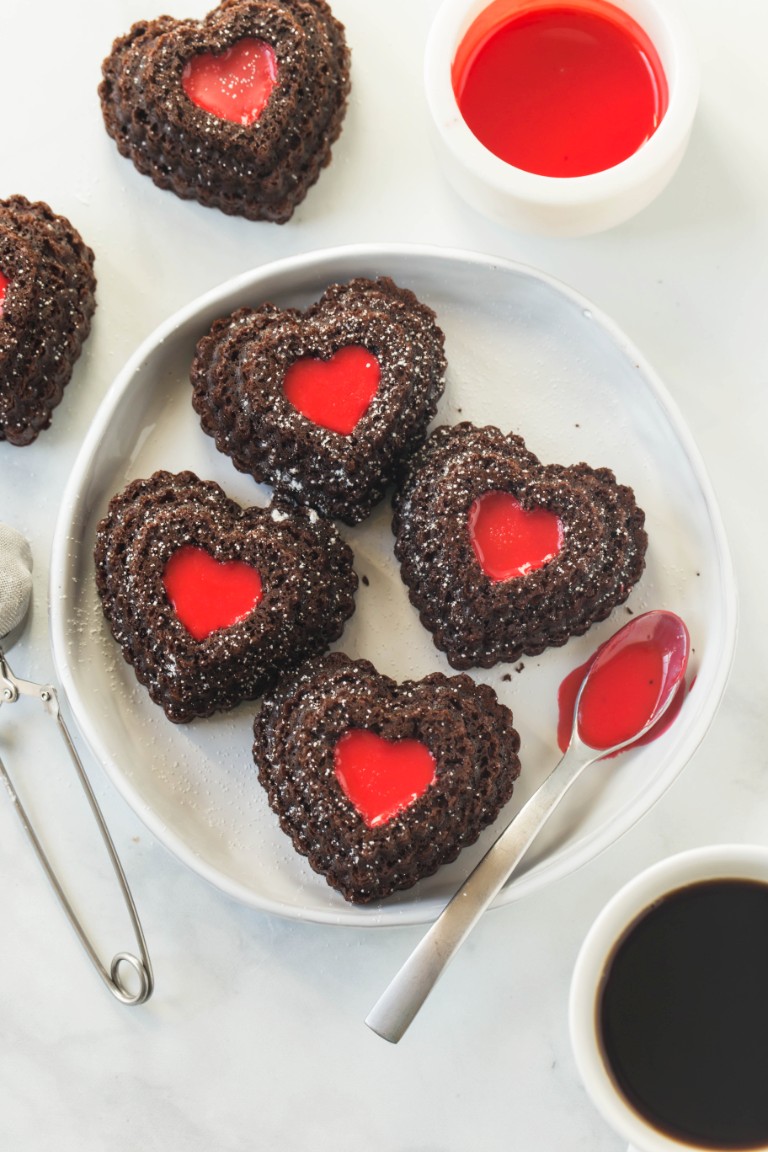 several chocolate heart shaped cupcakes with red icing filing on white plate