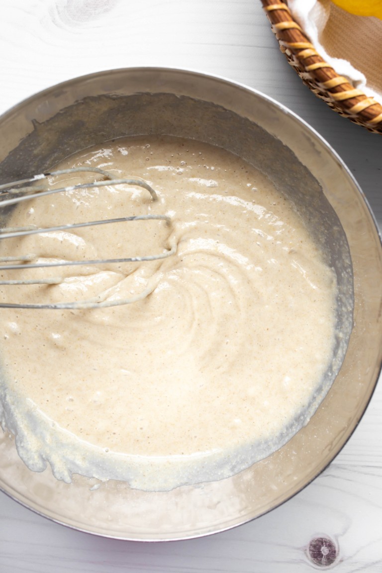 whisk running through wet lemon cake batter in metal bowl