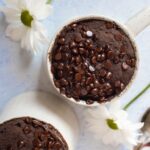overhead view of 2 cooked chocolate mug cakes with white flowers beside them