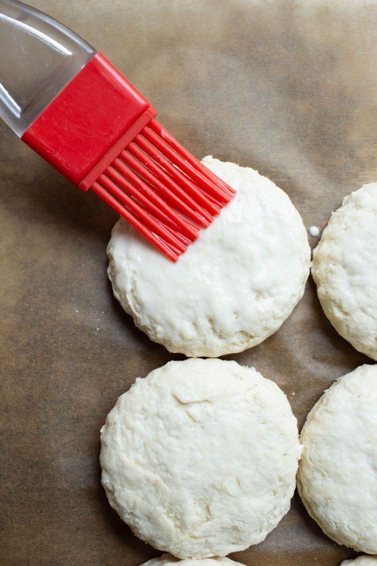 red brush brushing coconut milk on tops of biscuits before baking