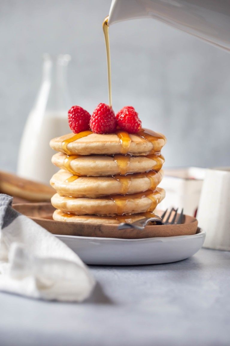 stack of vegan pancakes on round wood plate with raspberries on top