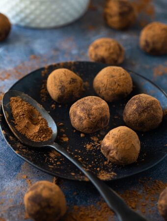 closeup of chocolate truffles on black plate with spoon of cocoa powder