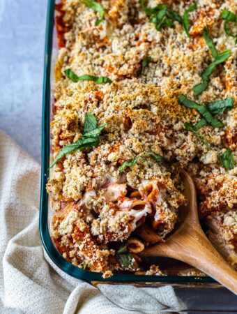 closeup of wooden spoon spooning out some baked ziti from casserole dish