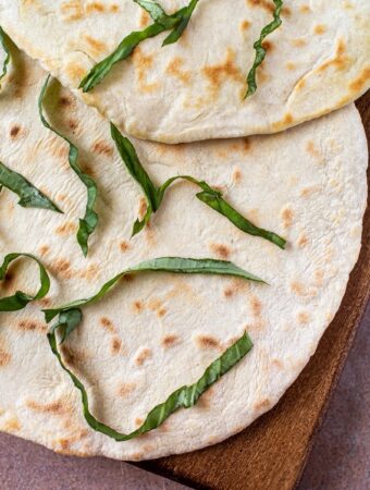 2 large pieces of vegan flatbread on wood platter with fresh basil on top