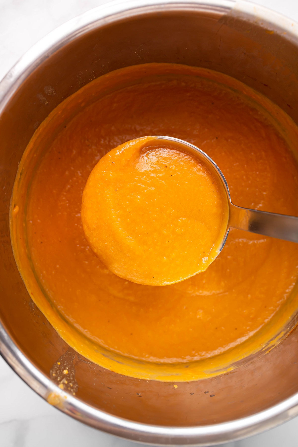 Silver ladle with sweet potato soup on it inside instant pot