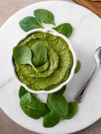 overhead image of white marble platter with bowl of vegan spinach pesto