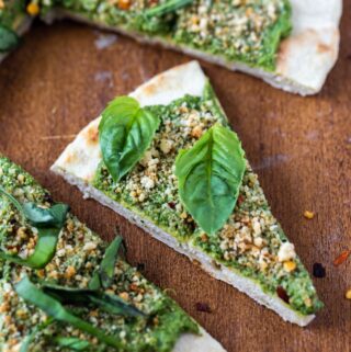 closeup of vegan pesto pizza slices on flatbread on wood platter